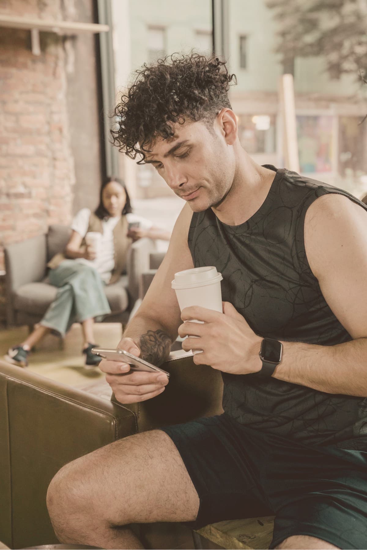 Homme dans un café, gobelet à emporter dans une main et téléphone dans l’autre